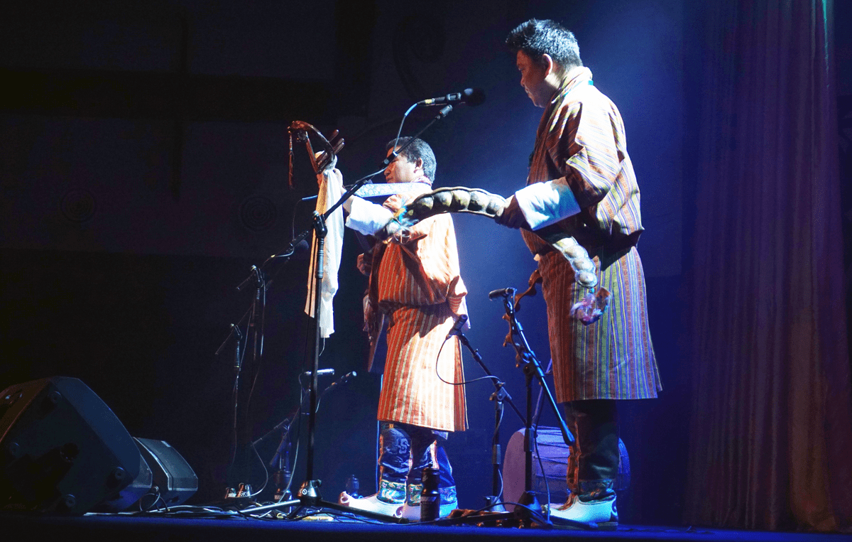 Two musicians on stage playing with one holding a pea pod-shaped shaker 
